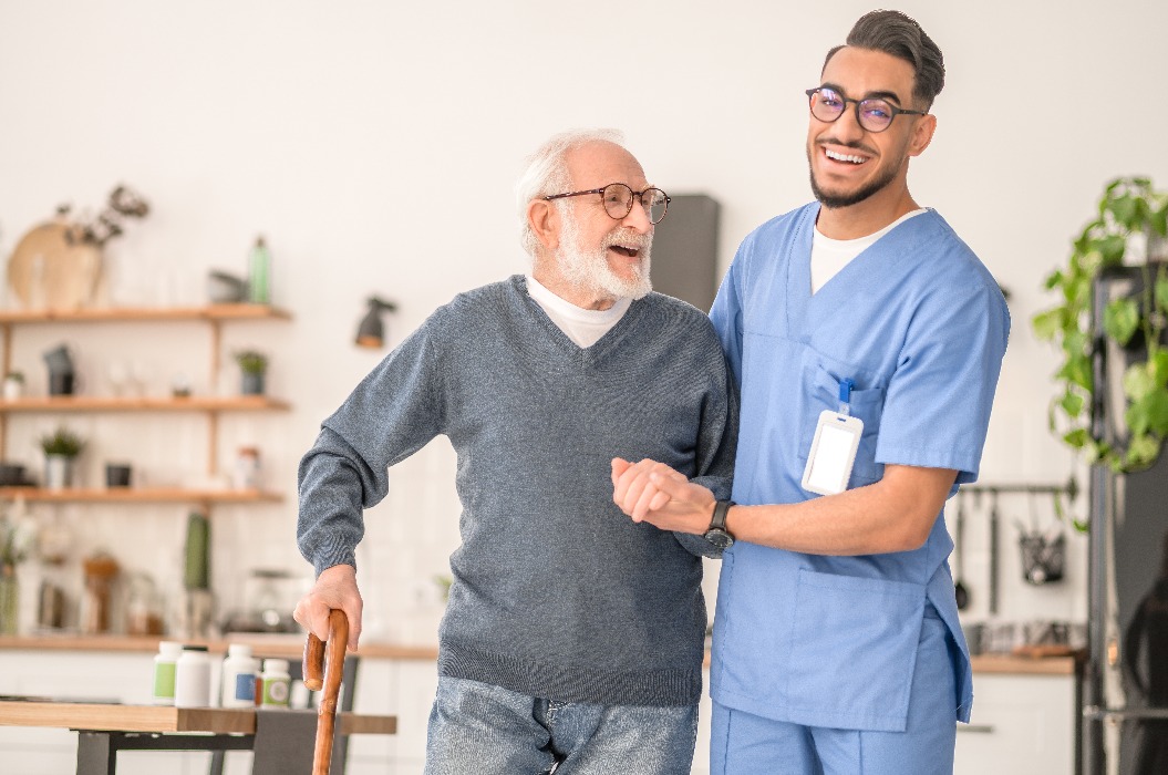 Krankenschwester hilft ihrem älteren Patienten beim Gehen mit einem Stock